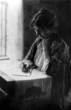 A woman seated at a table, writing.