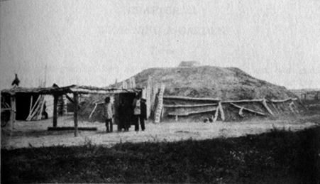 people standing in front of a large earthen mound structure ringed by pieces of wood