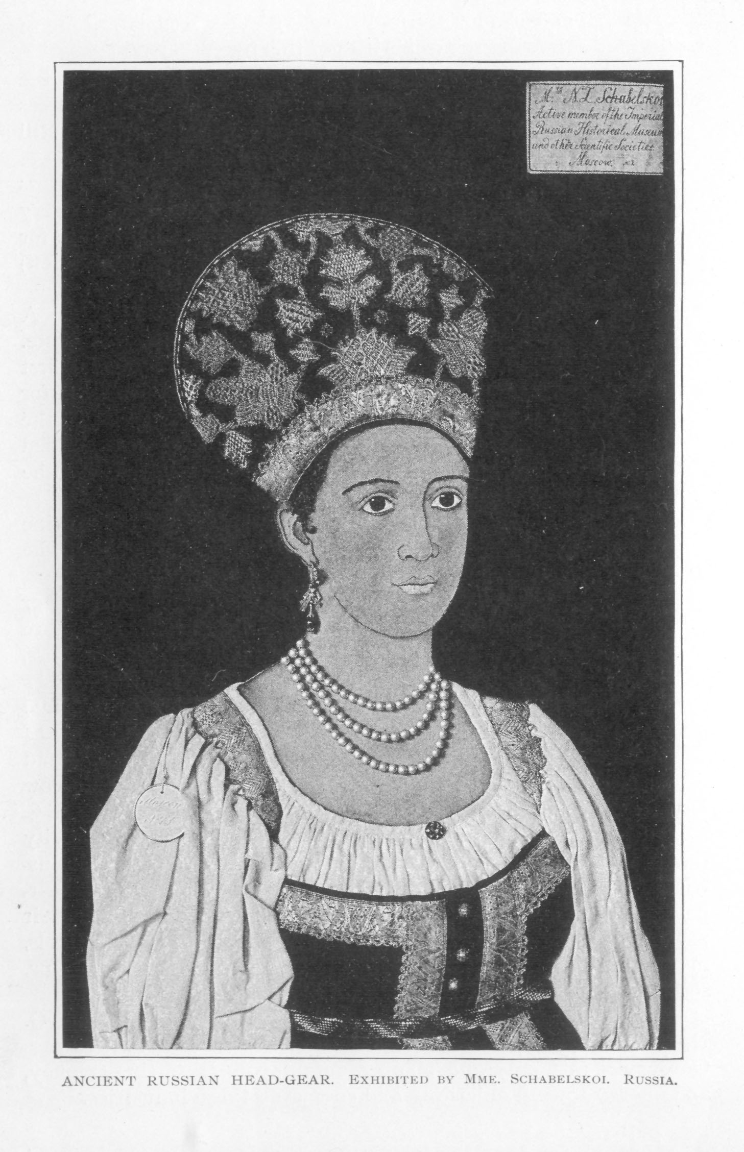 large emboidered headdress on display with traditional dress and pearl necklace