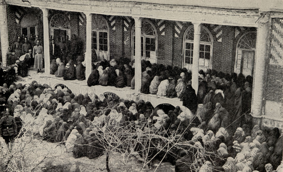 a crowd of people, seated shoulder to shoulder, waiting in a veranda and yard