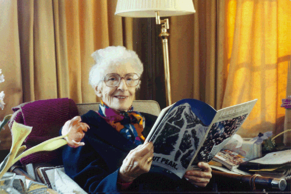 May Sarton, a cheerful elder woman, seated reading