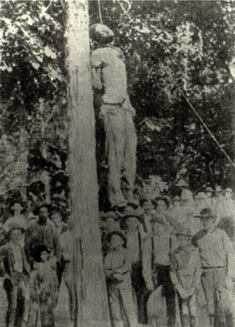 black man hanged from a tree as a crowd of white men and boys looks on